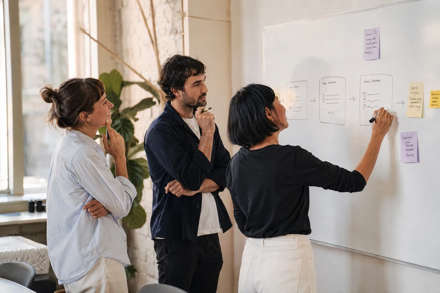 Three teammates discussing a hand-drawn flow at a whiteboard.