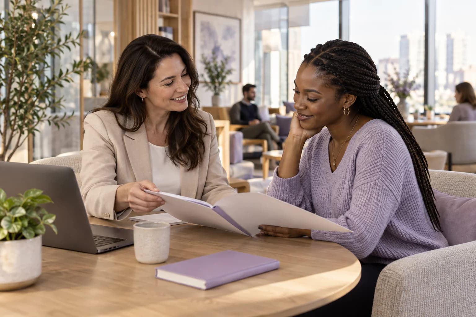 An HR colleague welcoming a new teammate and reviewing a welcome folder in a bright office lounge.